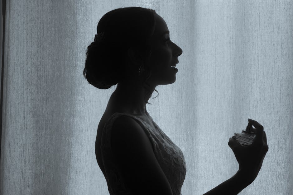 Silhouette of a woman in profile holding a perfume bottle against a curtain backdrop.
