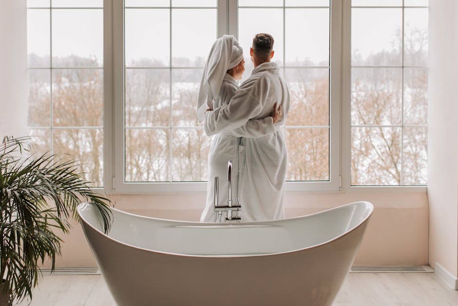Couple in bathrobes standing by a window overlooking a snowy landscape.