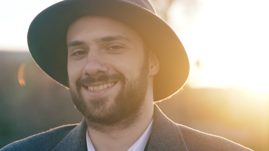 A smiling man wearing a hat and coat outdoors.