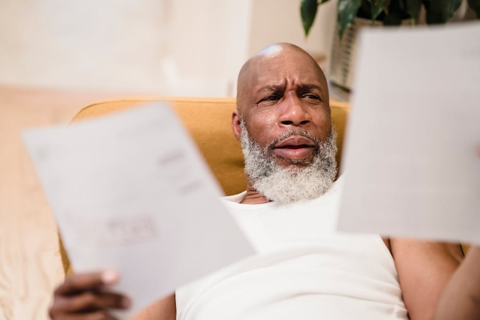A middle-aged man looks concerned as he reviews household bills, sitting in a comfortable chair indoors.