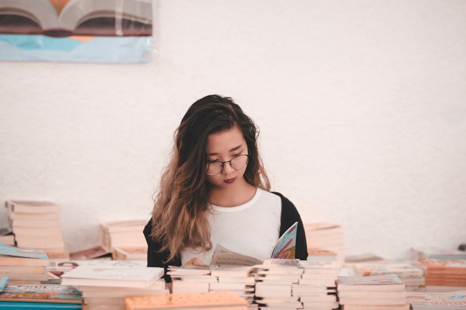 Asian woman engrossed in reading, surrounded by books in an indoor setting.