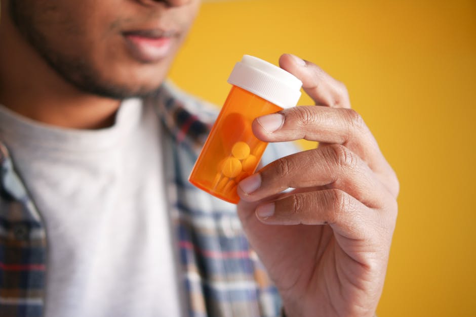 Close-up of a man holding a prescription medicine container against a yellow background.