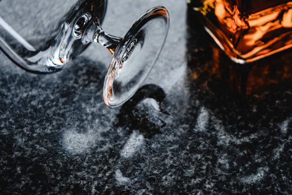 A close-up shot showcasing a cognac glass and bottle on a textured marble surface.