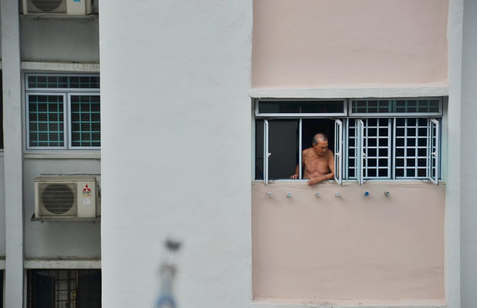 Elderly man gazing from an urban high-rise window, evoking solitude.