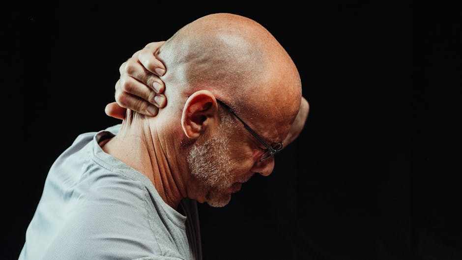 Side view of a man holding his neck in pain against a black background.