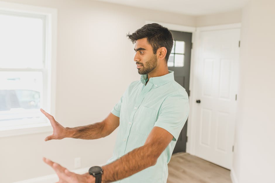Man gesturing during a conversation in a bright modern room, wearing a light blue polo shirt.