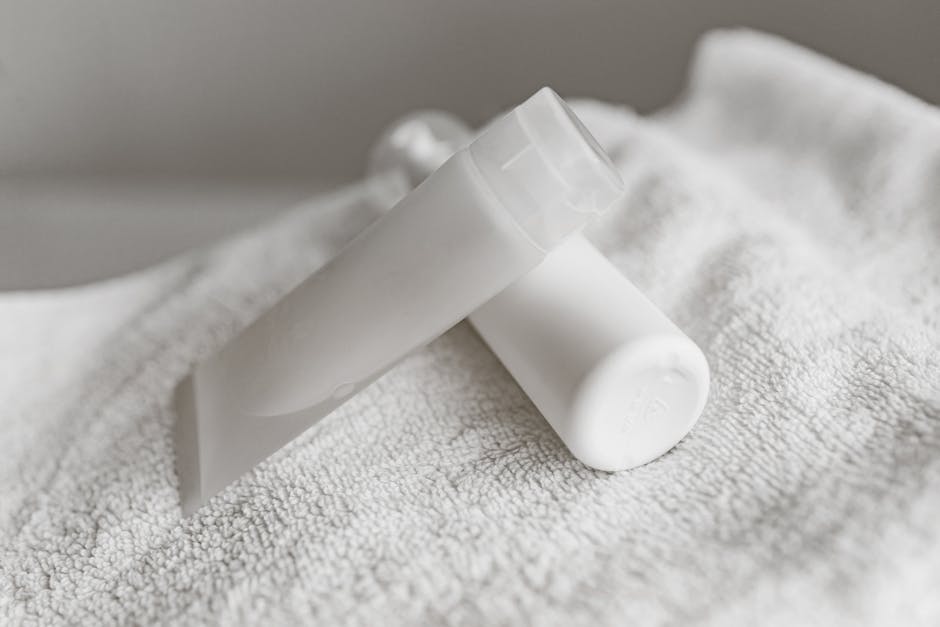 Close-up of white cosmetic tubes on a soft towel, showcasing minimalist skincare packaging.