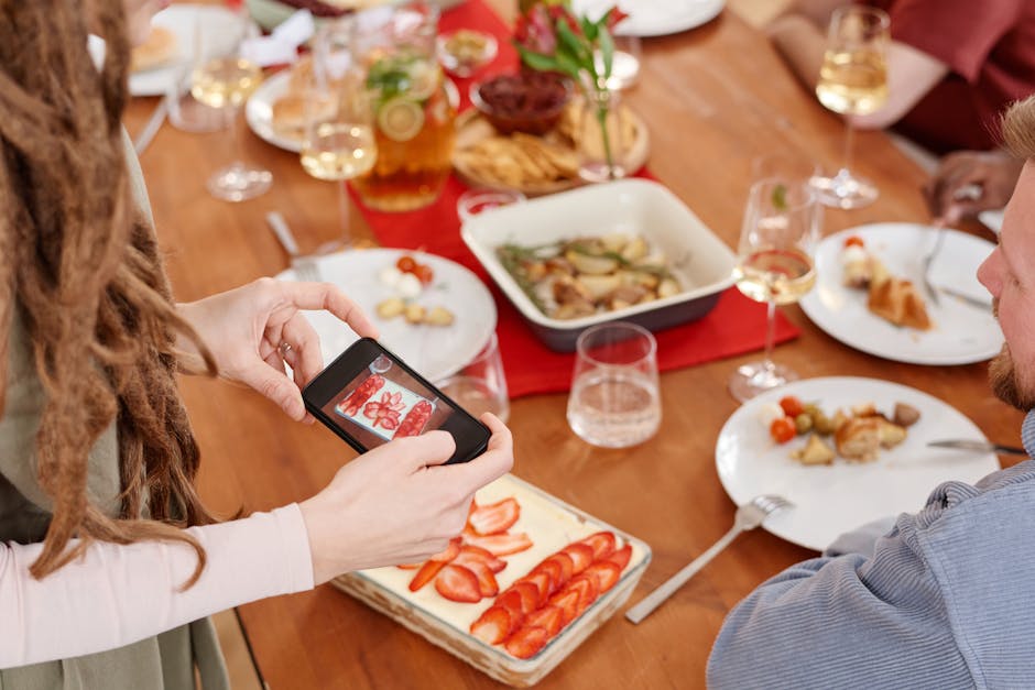 A person captures a photo of strawberry tiramisu at a lively dinner gathering.